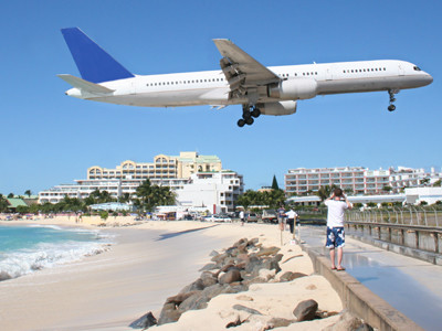 Ein Flugzeug im Landeanflug fliegt tief über einem Spaziergänger auf einer Strandpromenade. © liveostockimages, Fotolia