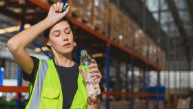 Eine ersch&ouml;pfte Arbeiterin in gelber warnweste schwitzt bei der Arbeit und trinkt aus einer Mineralwasserflasche