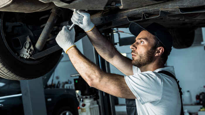 Kfz-Mechaniker arbeitet am Unterboden eines Autos