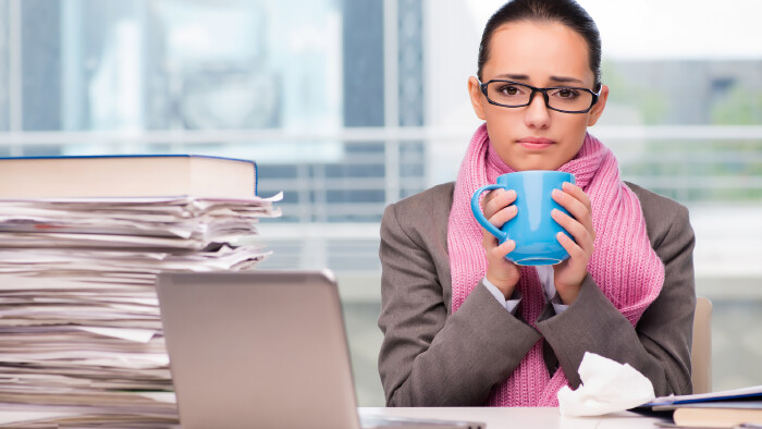 Kranke Frau sitzt mit einer Tasse Tee im Büro