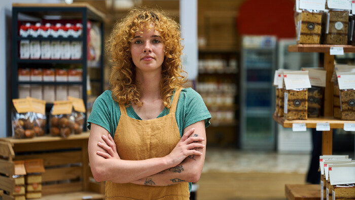 Selbstbewusste Verkäuferin steht mit verschränkten Armen im Supermarkt.