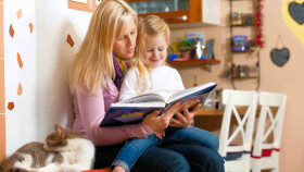 Mutter und Kind beim Vorlesen - mit Katze auf der Ofenbank
