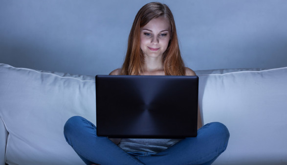 Teenager sitzt mit Laptop auf der Couch