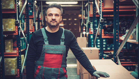 Arbeiter steht in einem Lager zwischen Regalen