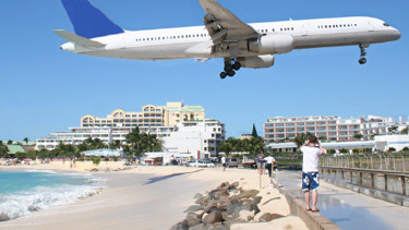 Ein Flugzeug im Landeanflug fliegt tief über einem Spaziergänger auf einer Strandpromenade.