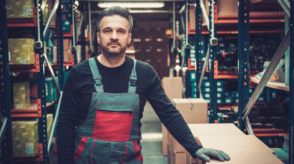 Arbeiter steht in einem Lager zwischen Regalen