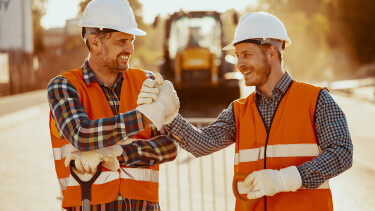 Zwei junge Arbeiter lächelnd auf der Baustelle
