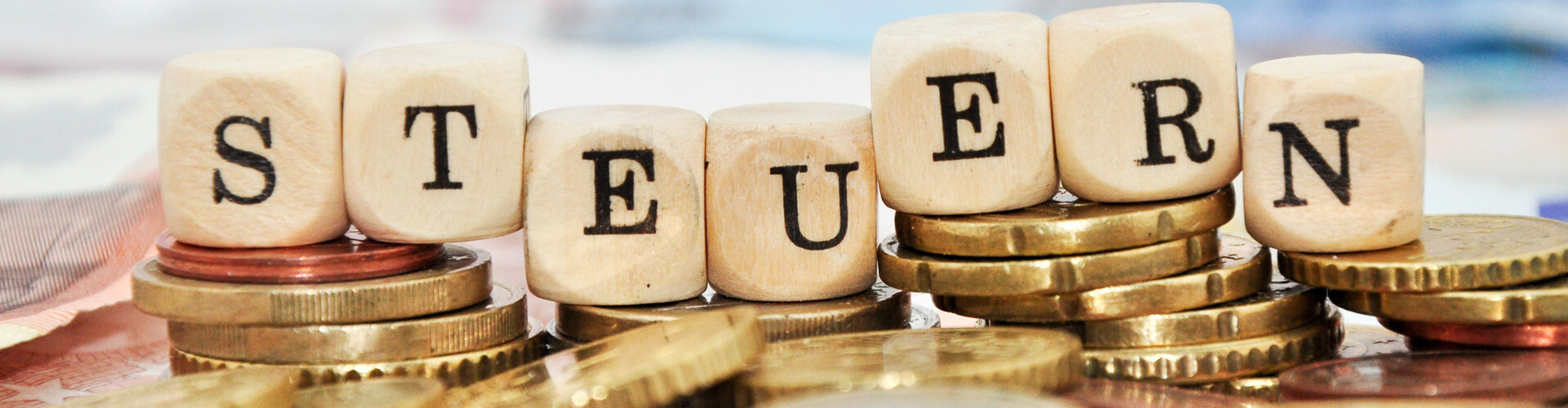 Buchstabenw&uuml;rfel, welche auf einem Stapel Euro-M&uuml;nzen liegen, bilden das Wort "Steuern"