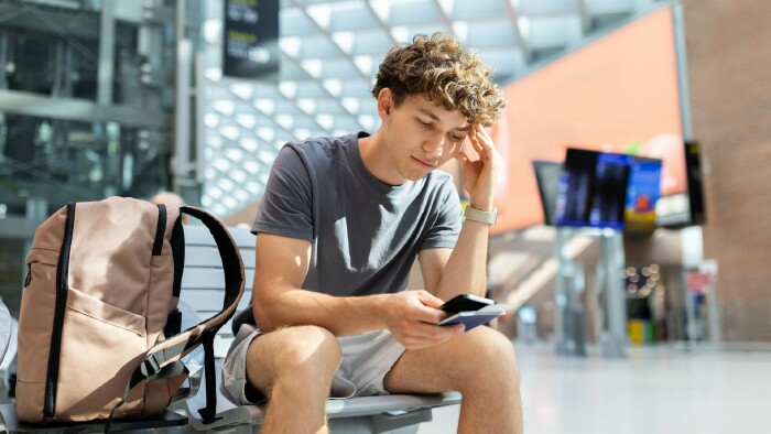 Junger Mann mit Rucksack sitzt am Flughafen