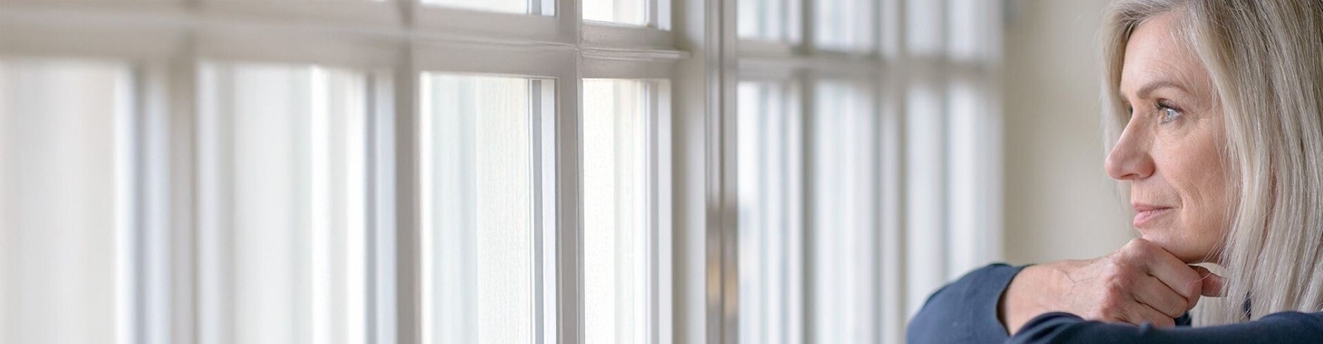 Reife, blonde Frau blickt traurig aus dem Fenster