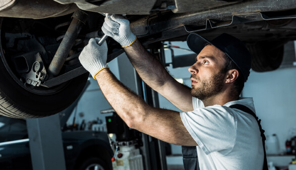 Kfz-Mechaniker arbeitet am Unterboden eines Autos