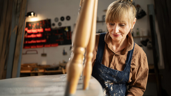 Eine &auml;ltere Tischlerin restauriert einen alten Stuhl.